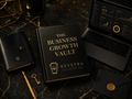 A black hardcover book titled 'The Business Growth Vault' with gold lettering and the brand name Keystra, styled on a dark marble surface with a laptop, notebook, pen, key, and envelope nearby.